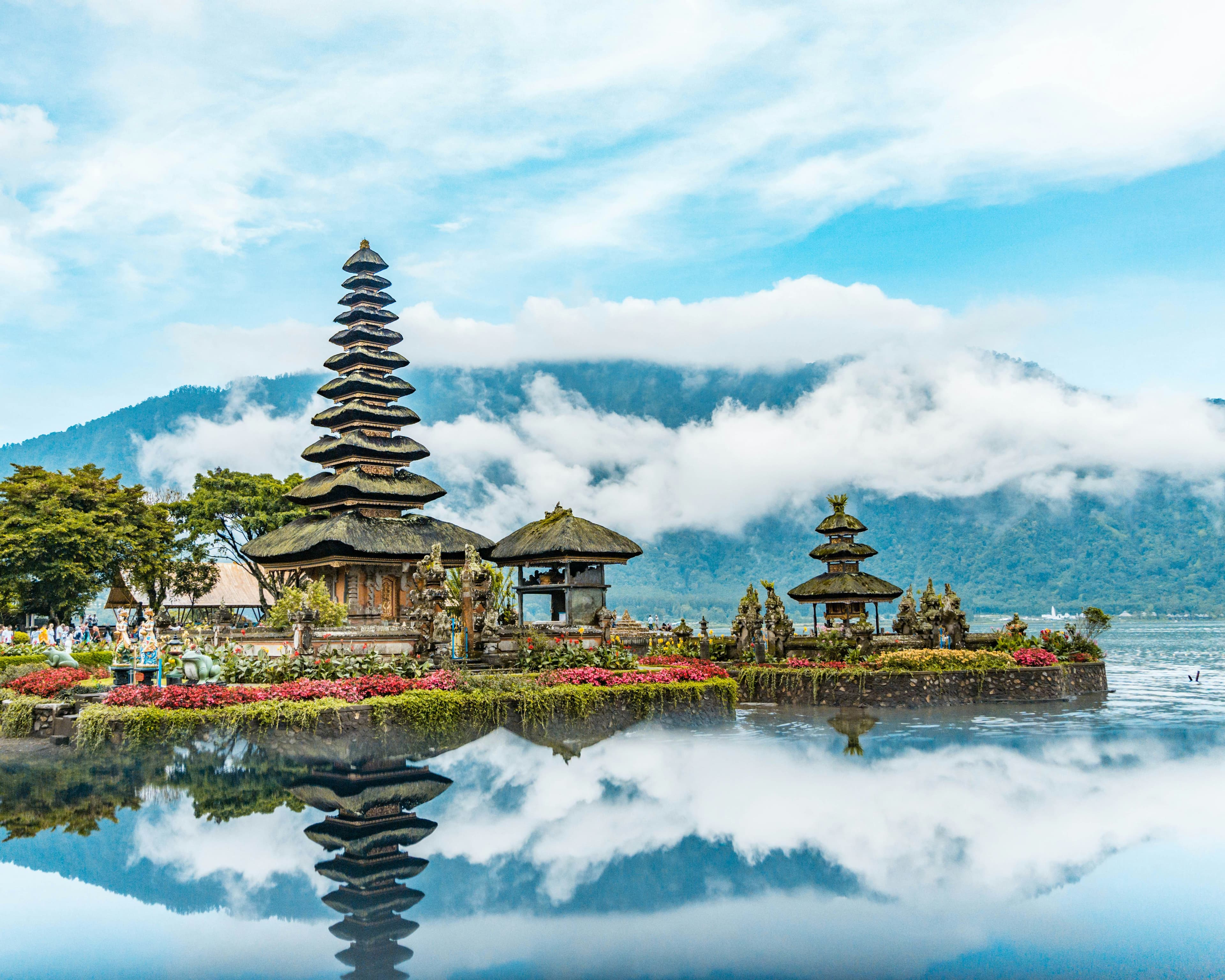 Balinese temple on a lake with mountains and clouds in the background.